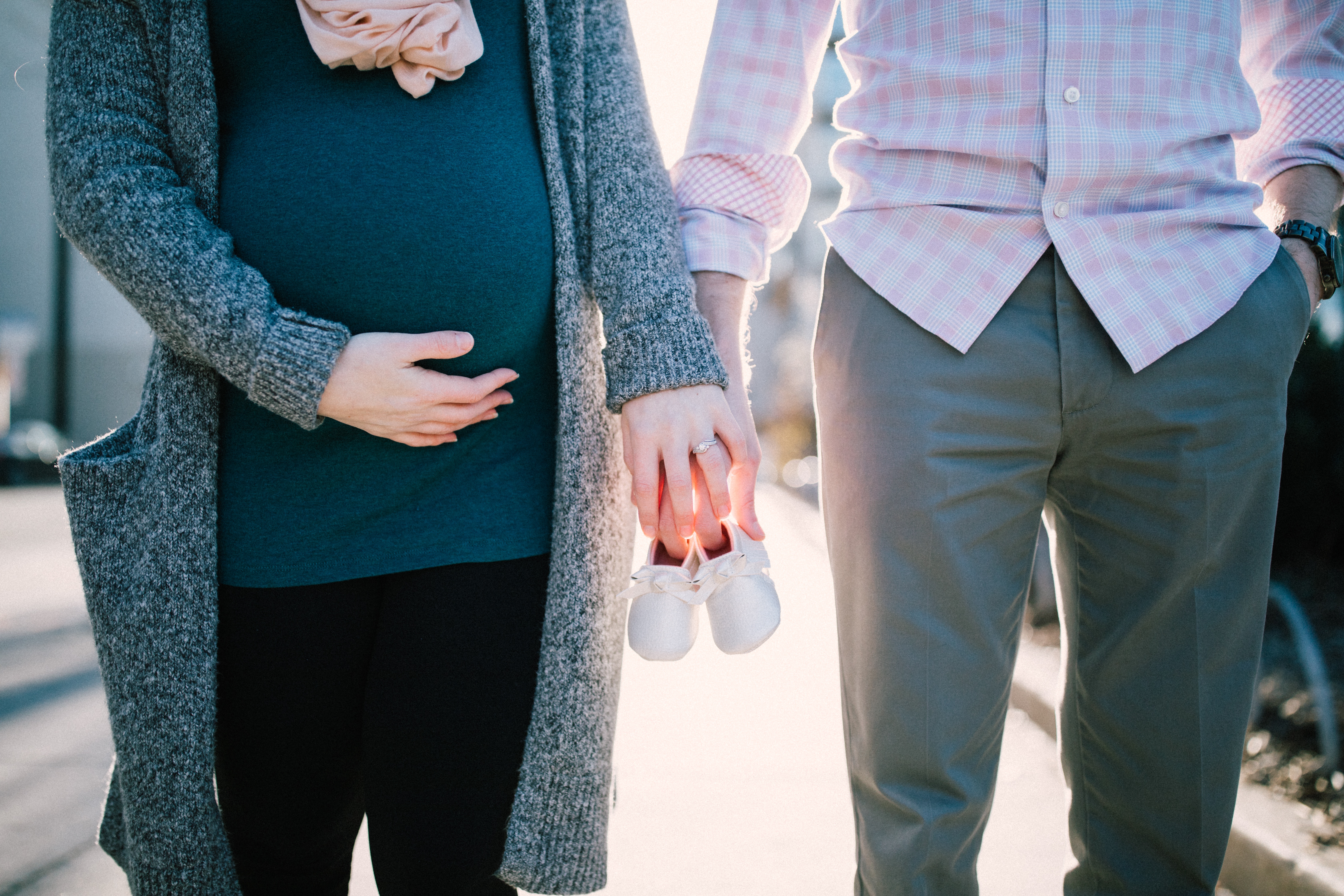 Pregnant Woman and Man holding Hands and Baby Shoes